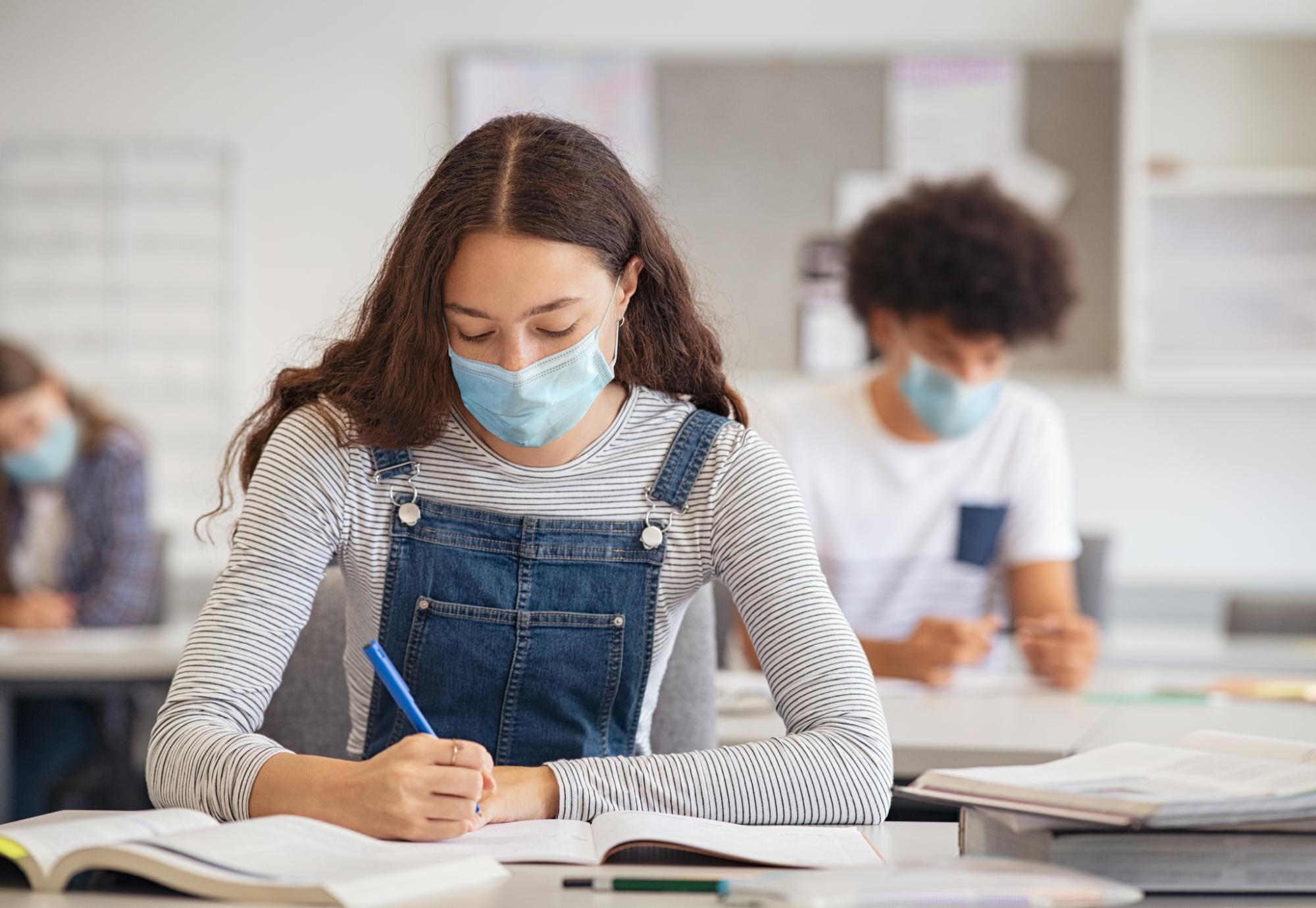 High school or college age girl in mask working at her desk