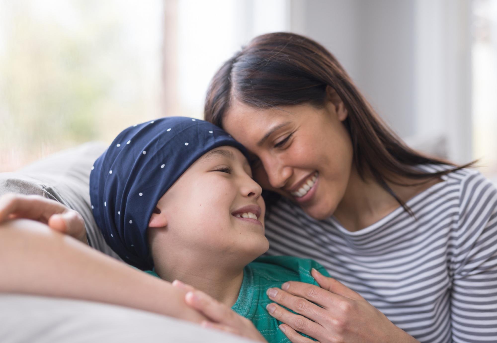 child with cancer smiling whilst hugging mother