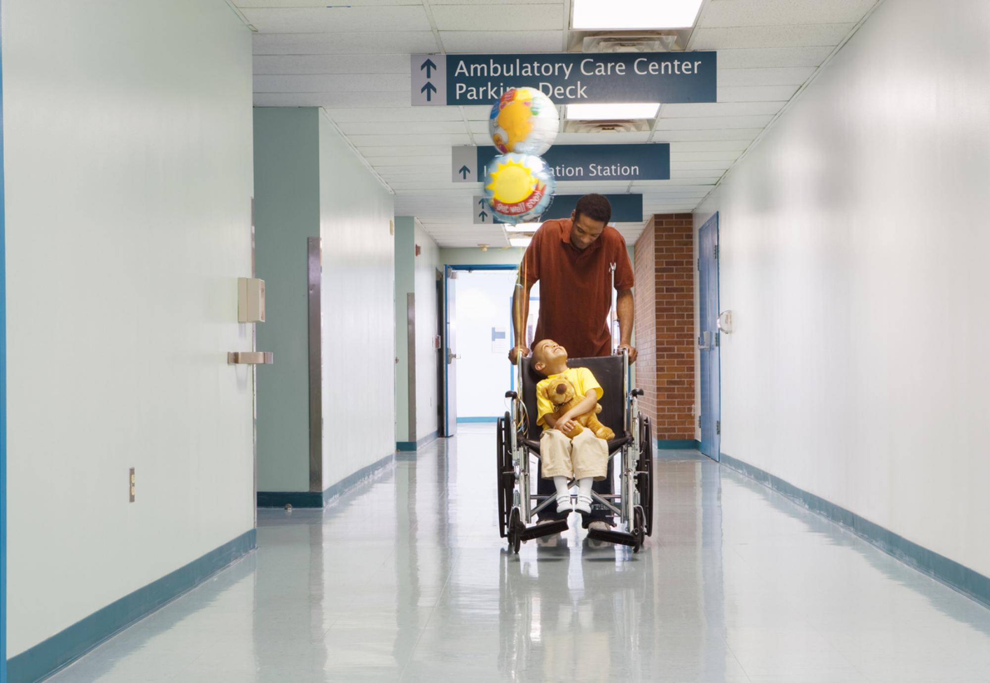 Man pushing boy in wheelchair through corridor