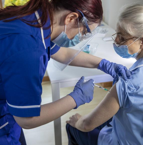 Nurse administering a vaccine jab to a colleague