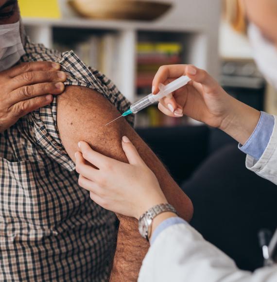 Older gentleman receiving a vaccine jab from a nurse