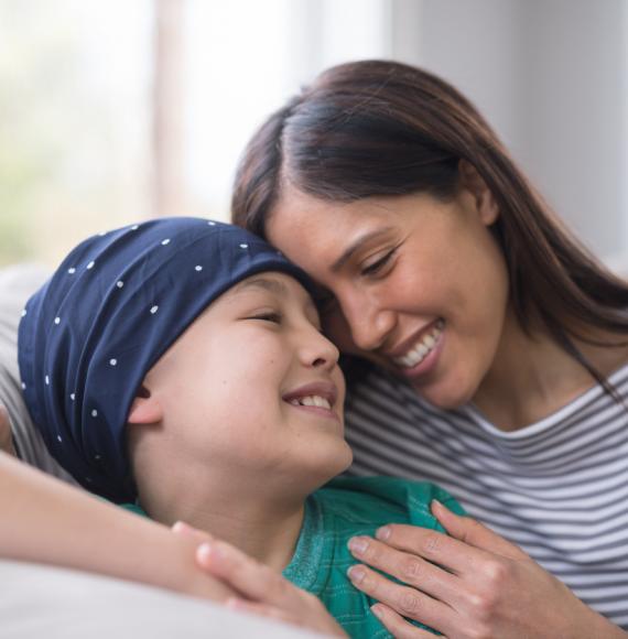 child with cancer smiling whilst hugging mother