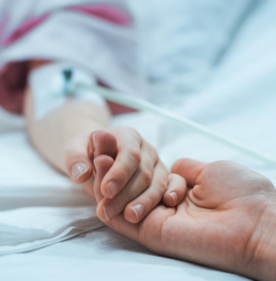 Close-up of a mother holding hands with her child as they recover in hospital