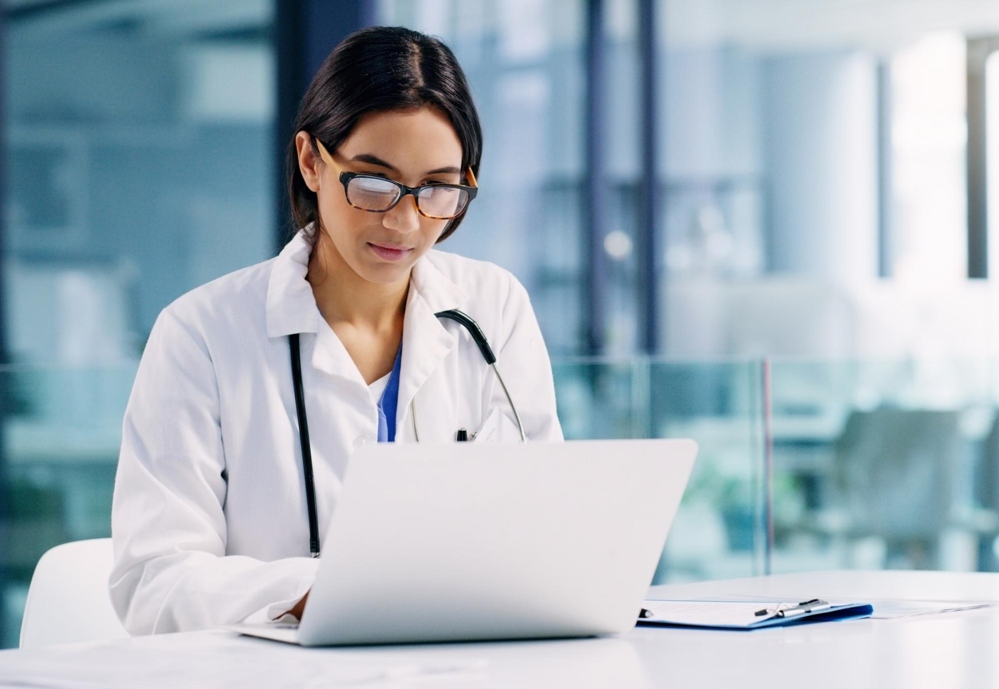 Female doctor looks at medical records on laptop.