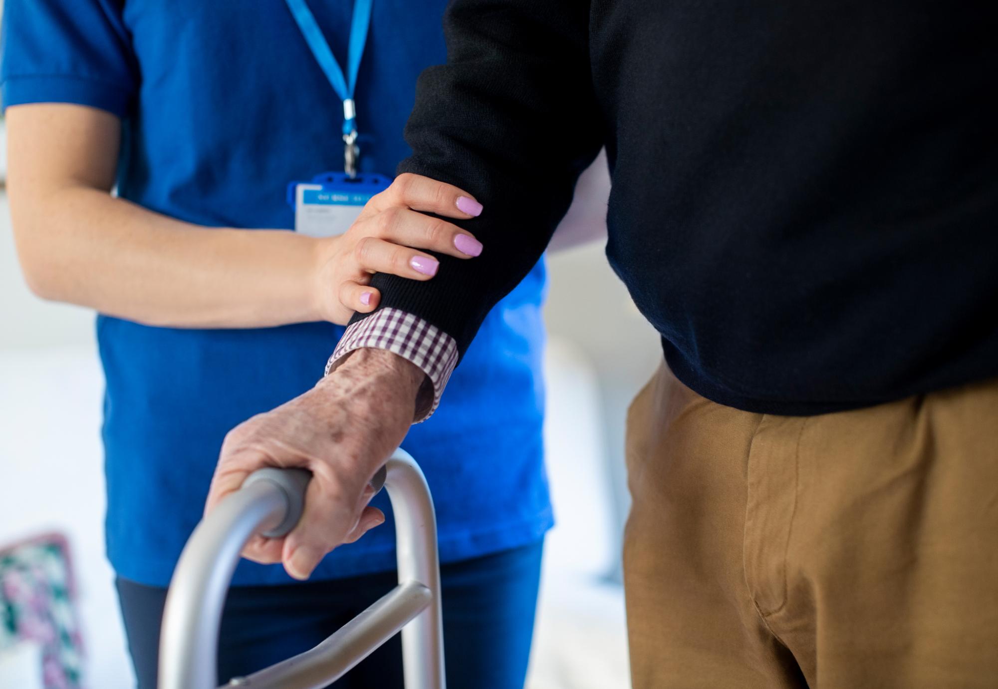 Community care worker supporting elderly person with zimmerframe