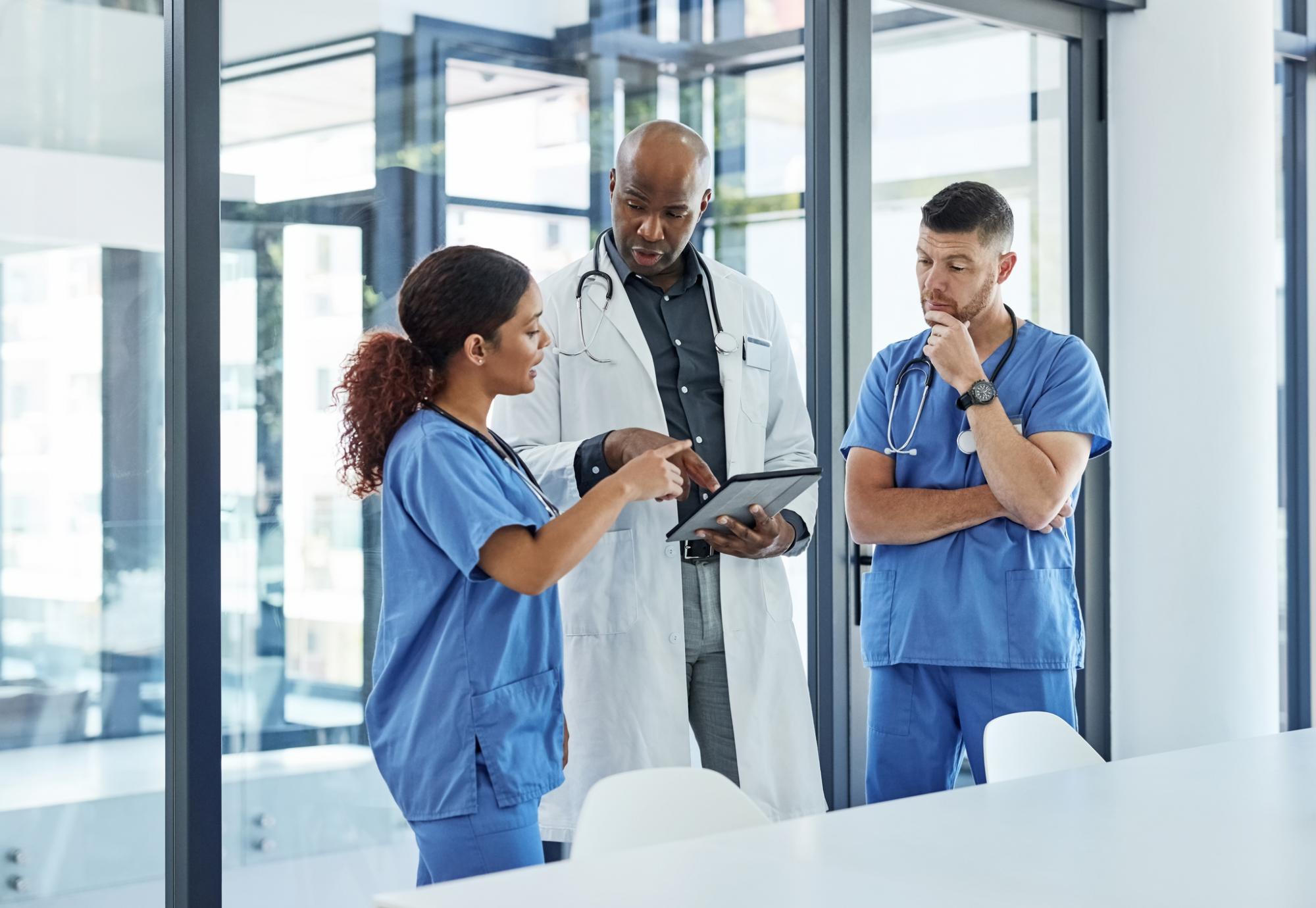 Doctor and two nurses discuss something on a tablet computer