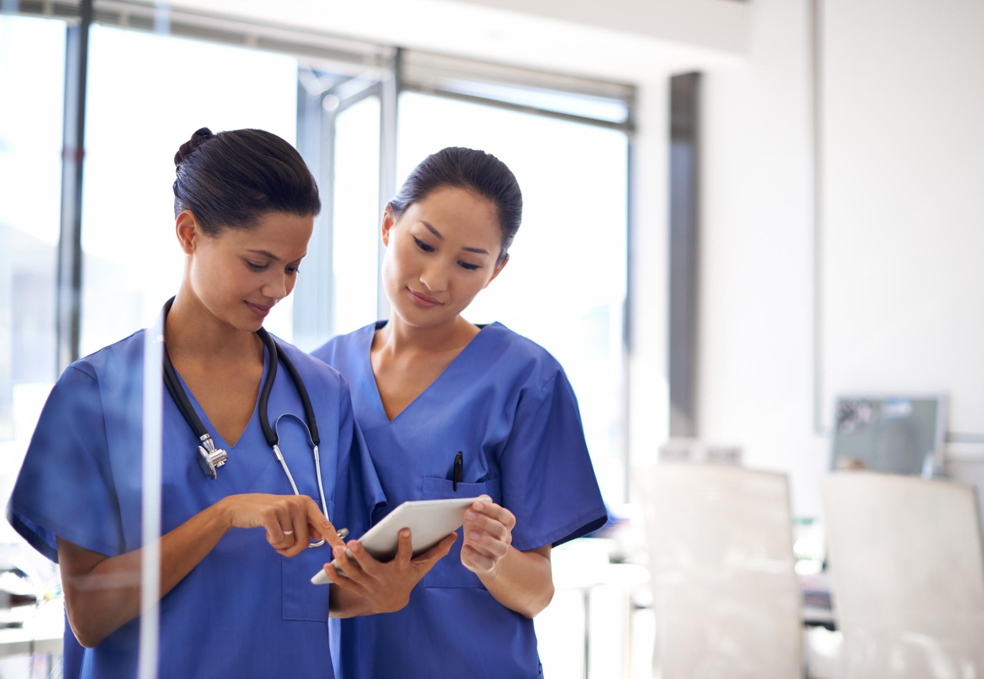 Two nurses discuss while reading a tablet computer