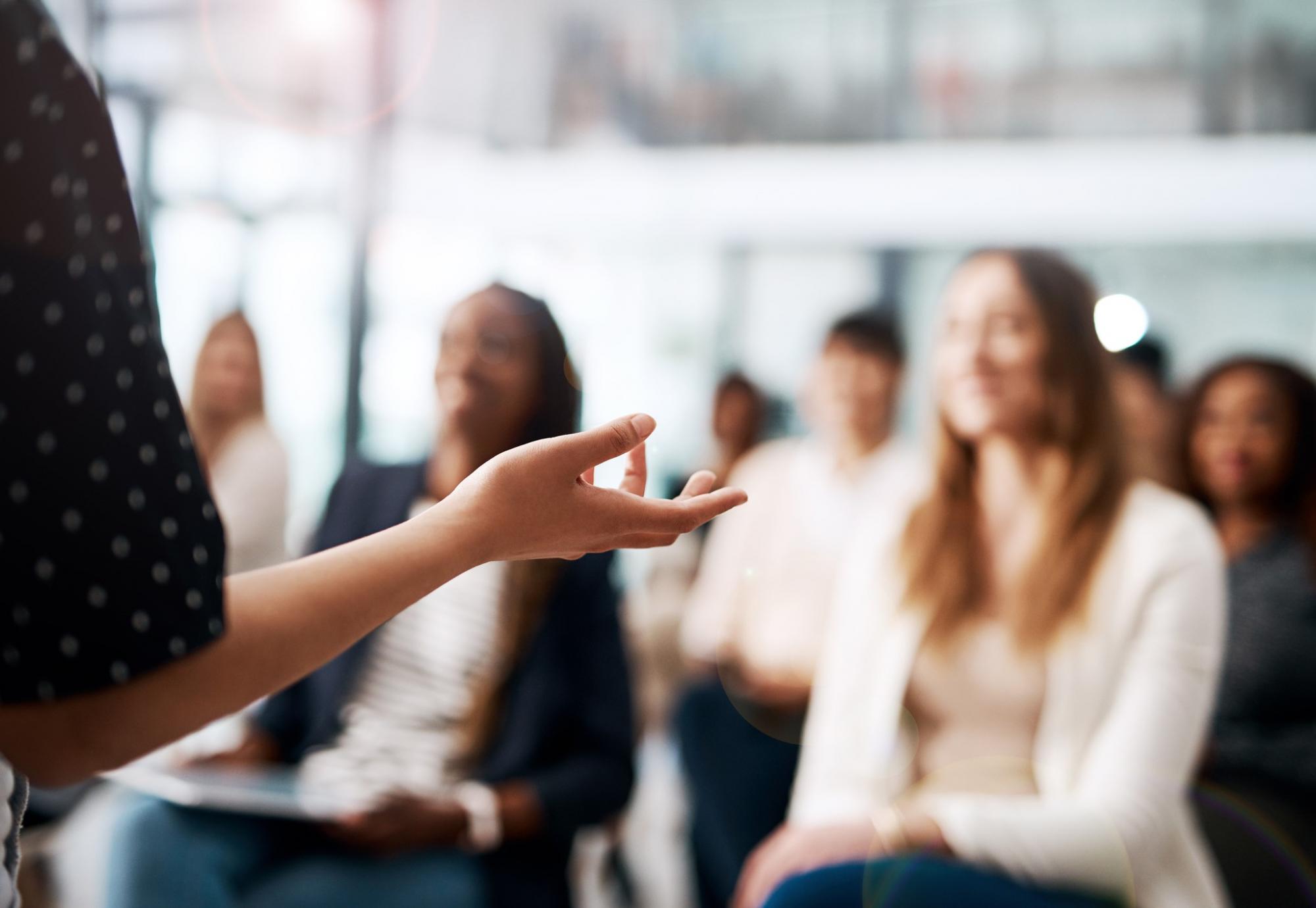 Off picture, woman presenting to a room of colleagues (in soft focus)