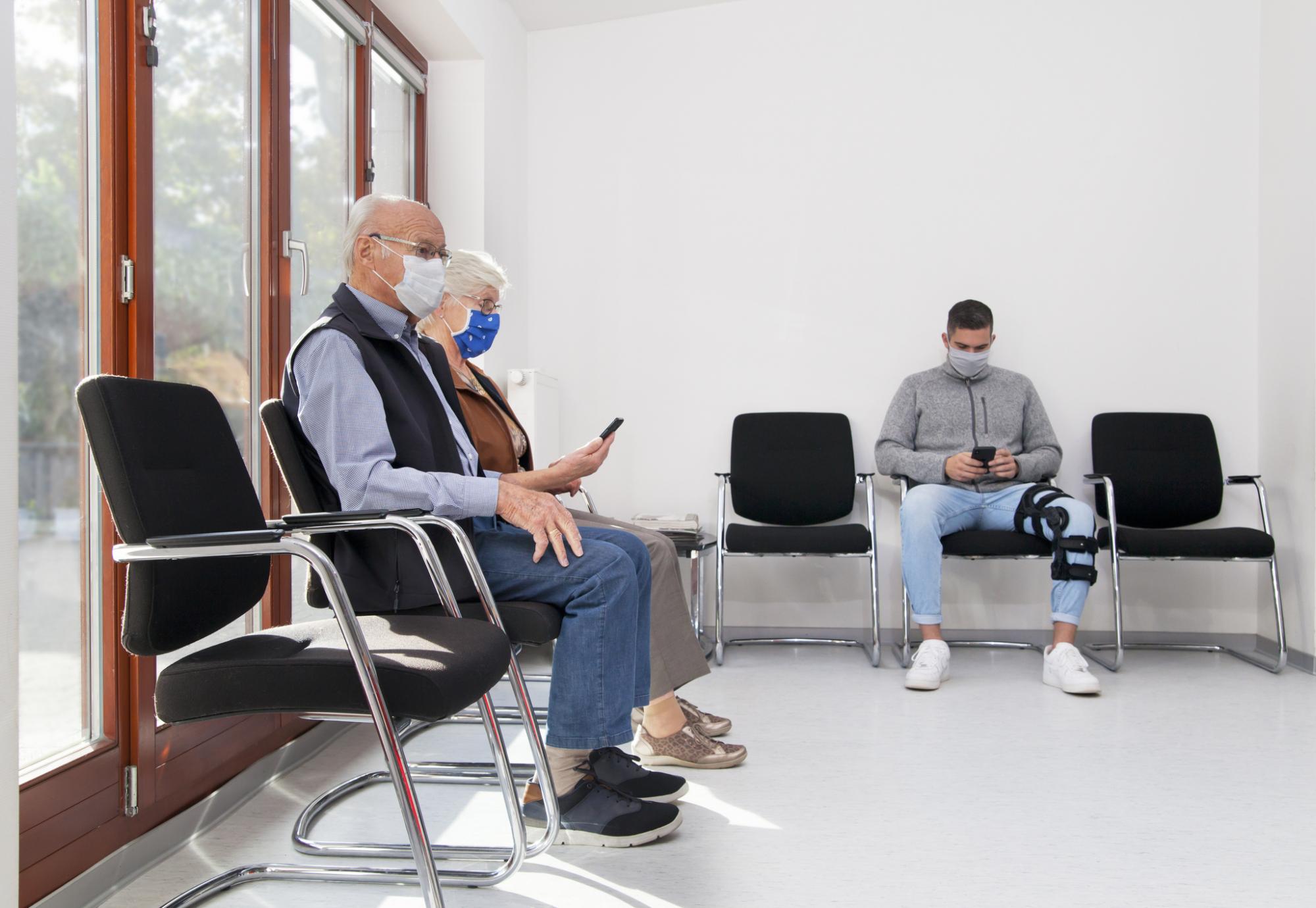 Elderly couple and a man sit in a GP waiting room