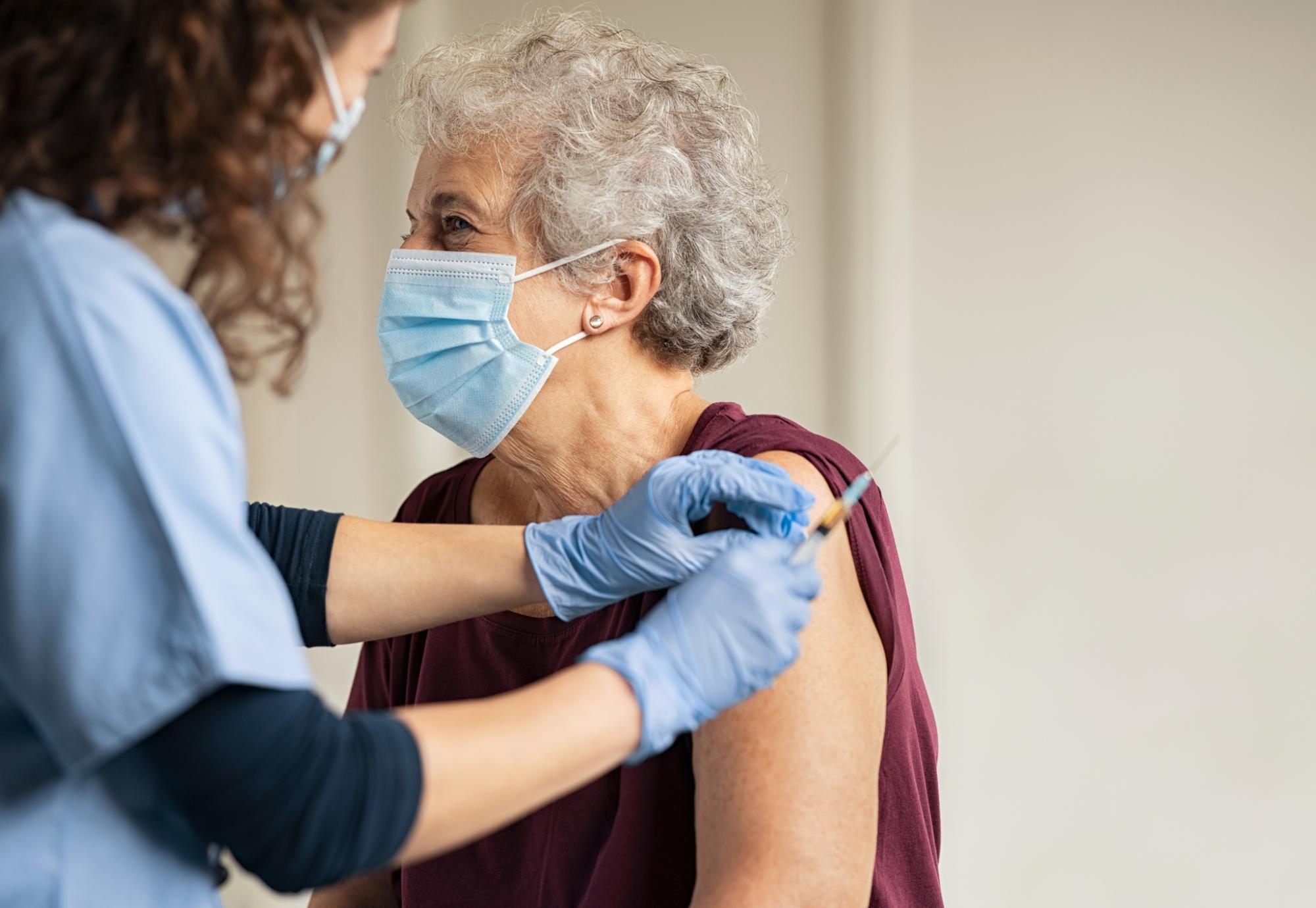 Elderly woman receiving a vaccine jab from a nurse