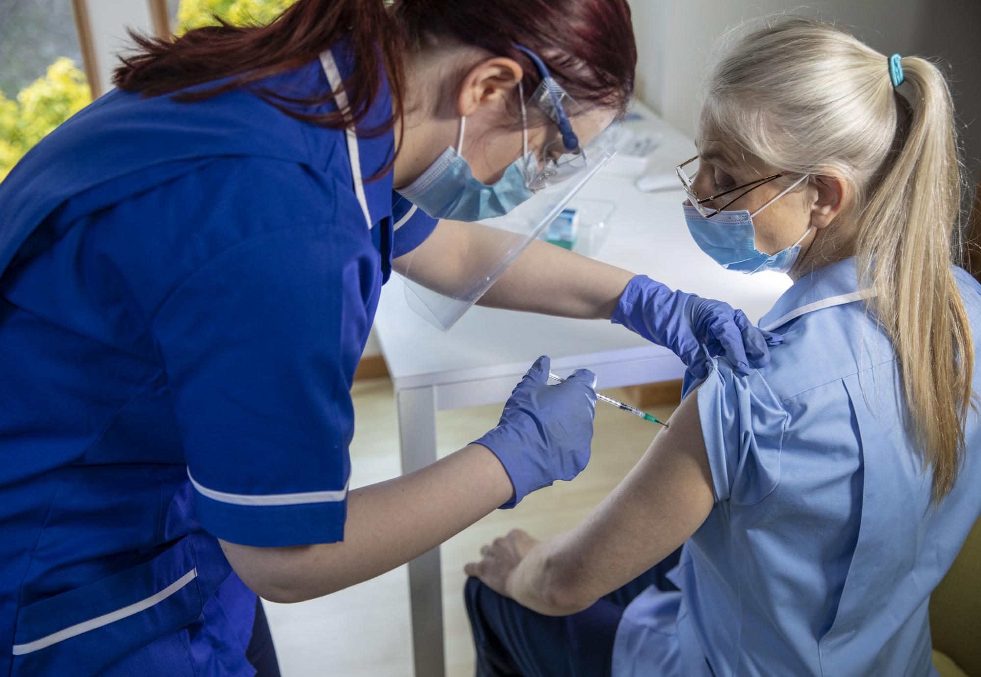 Nurse administering a vaccine jab to a colleague