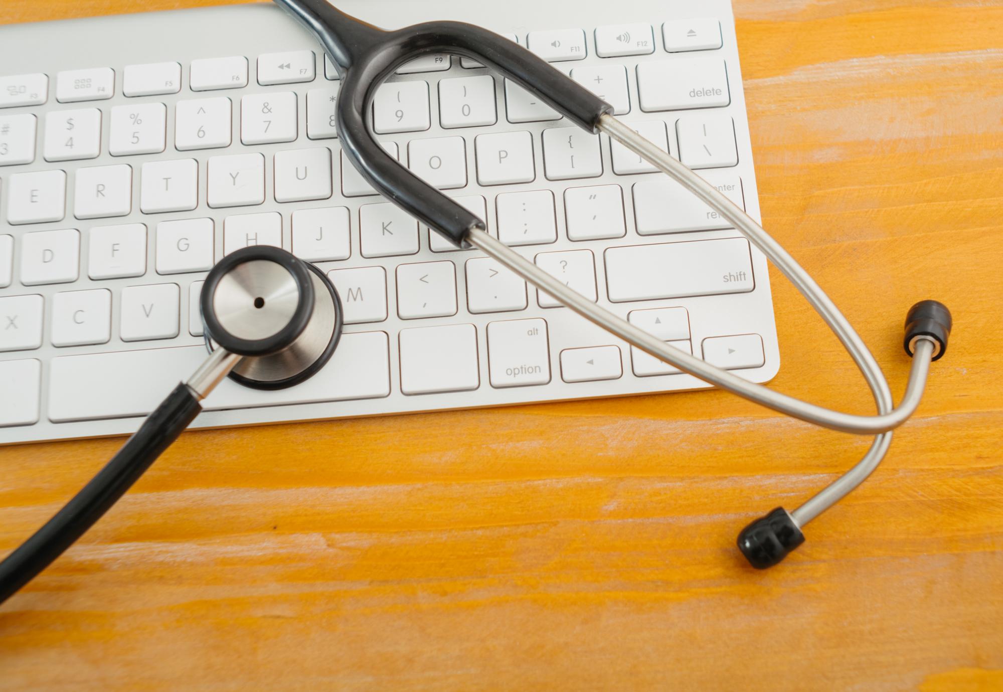 Stethoscope over computer keyboard on orange background