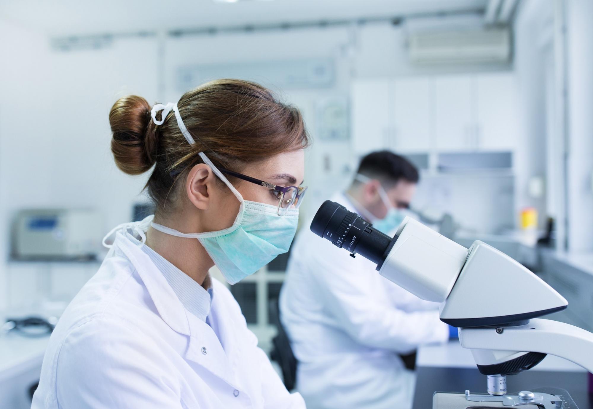 Microbiologist looking down a microscope in a lab