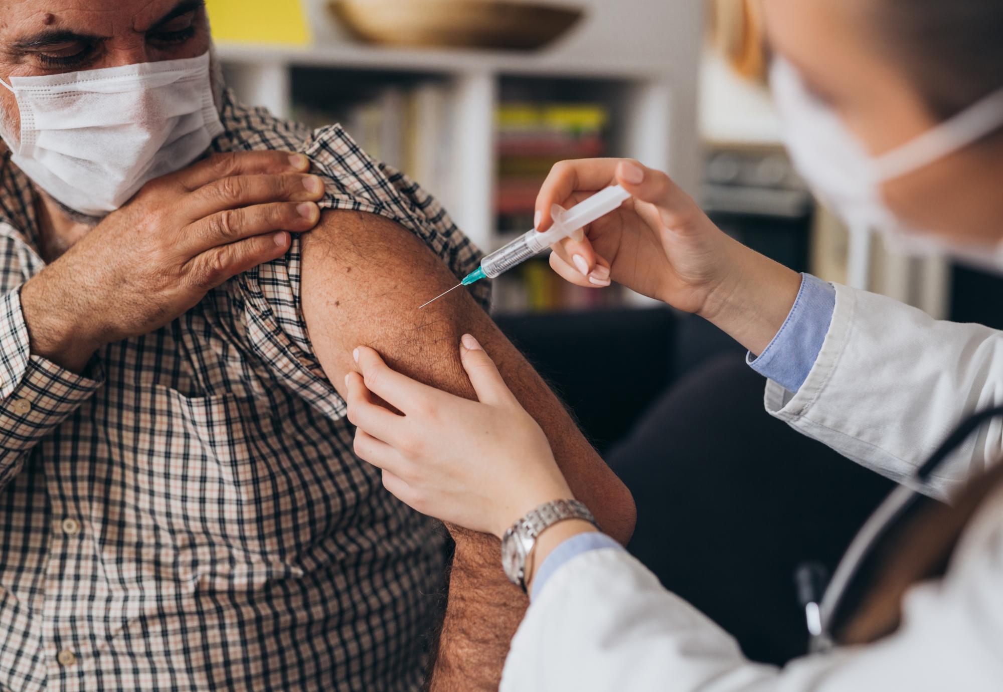 Older gentleman receiving a vaccine jab from a nurse