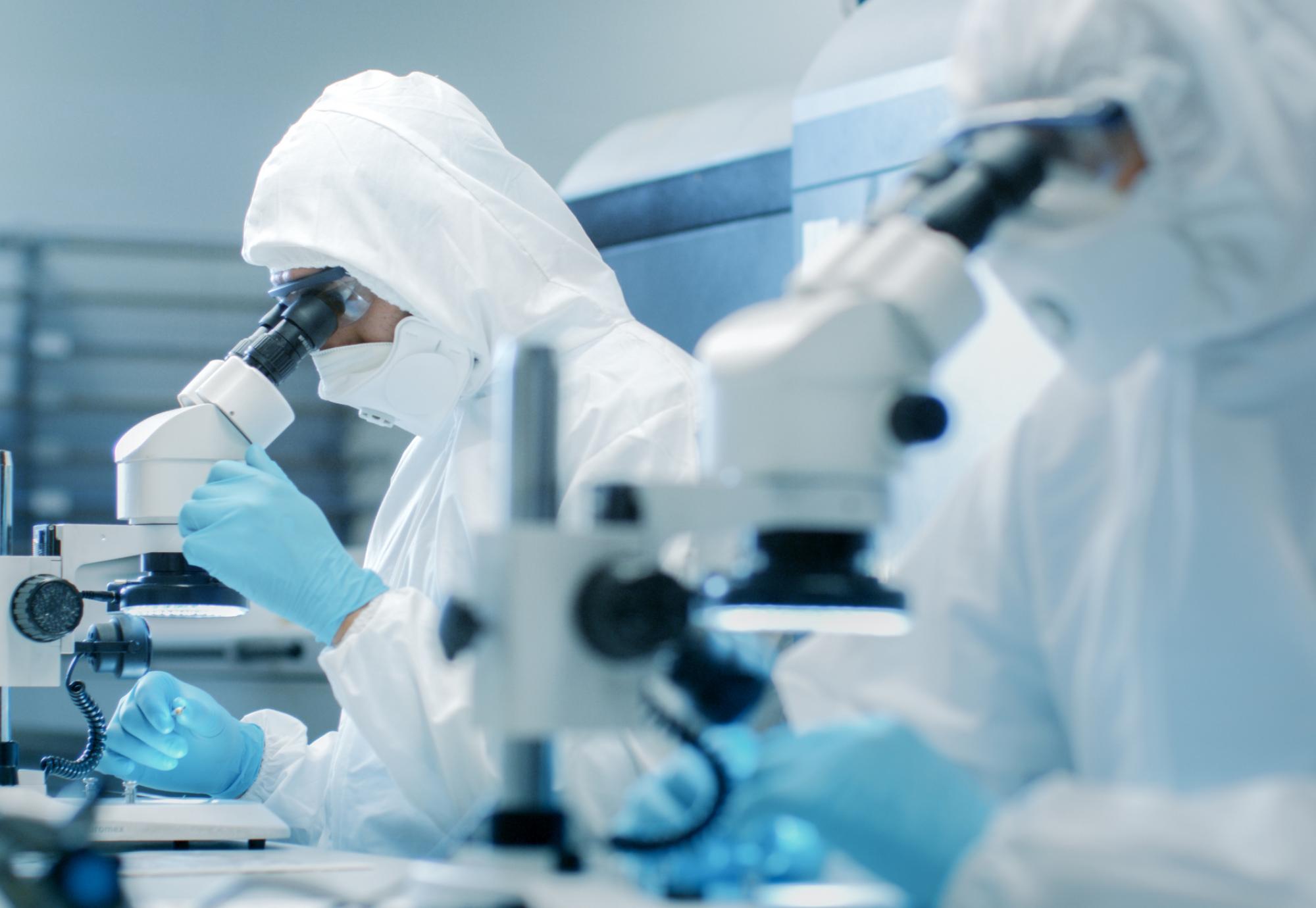 Two scientists in suits and a clean room testing pharmaceutical products