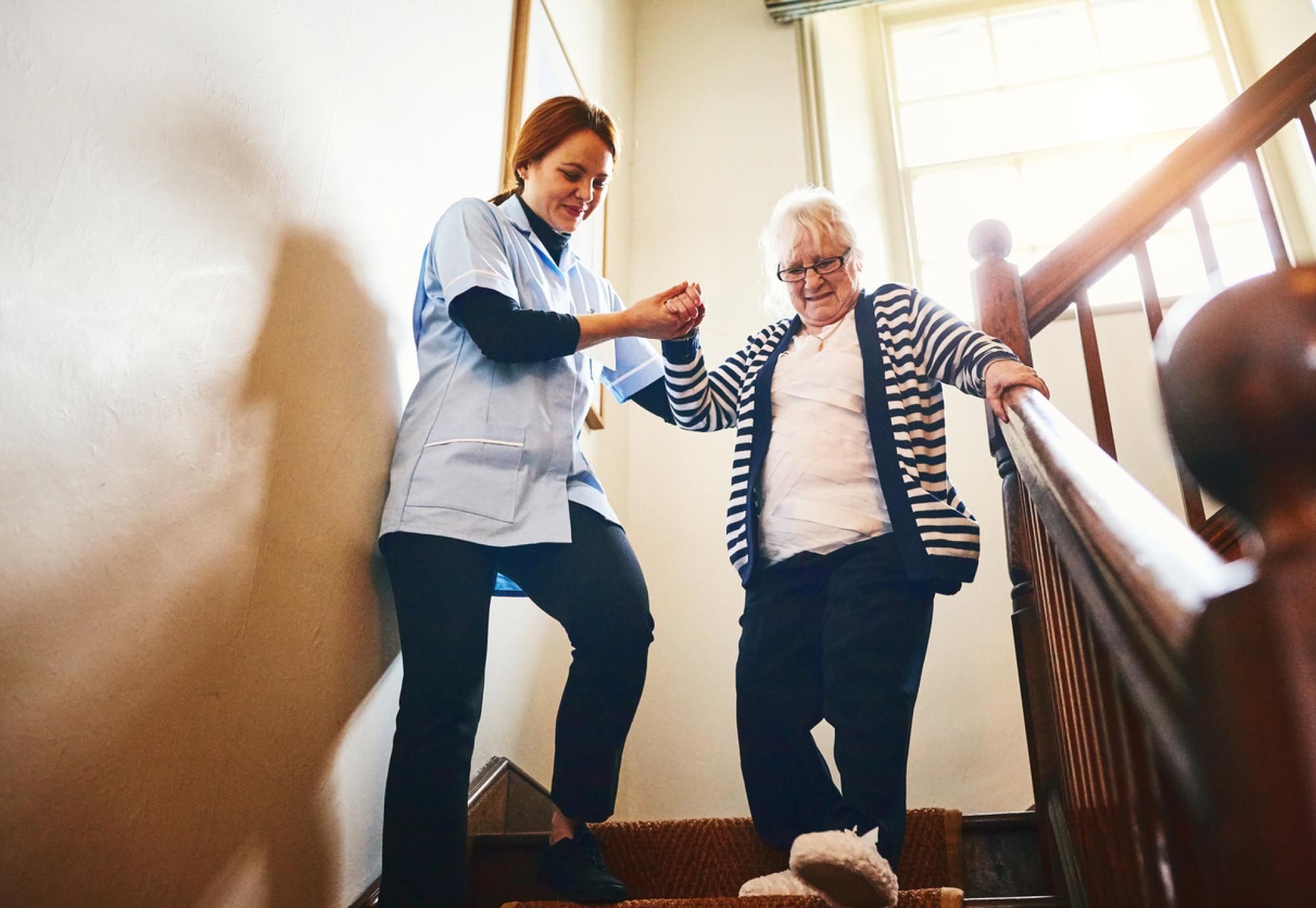 Carer helping elderly lady down the stairs