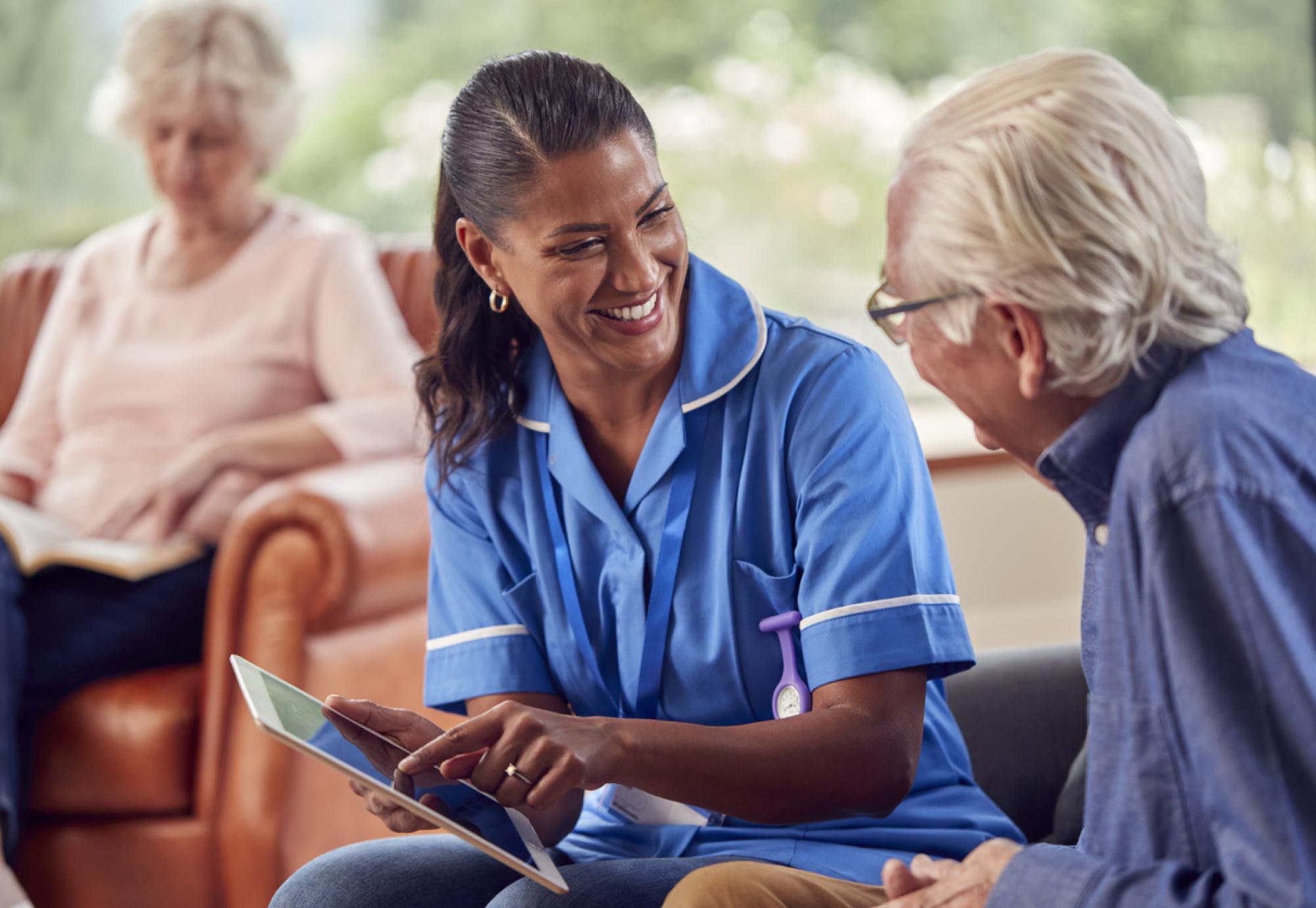 Senior Couple At Home With Man Talking To Female Nurse