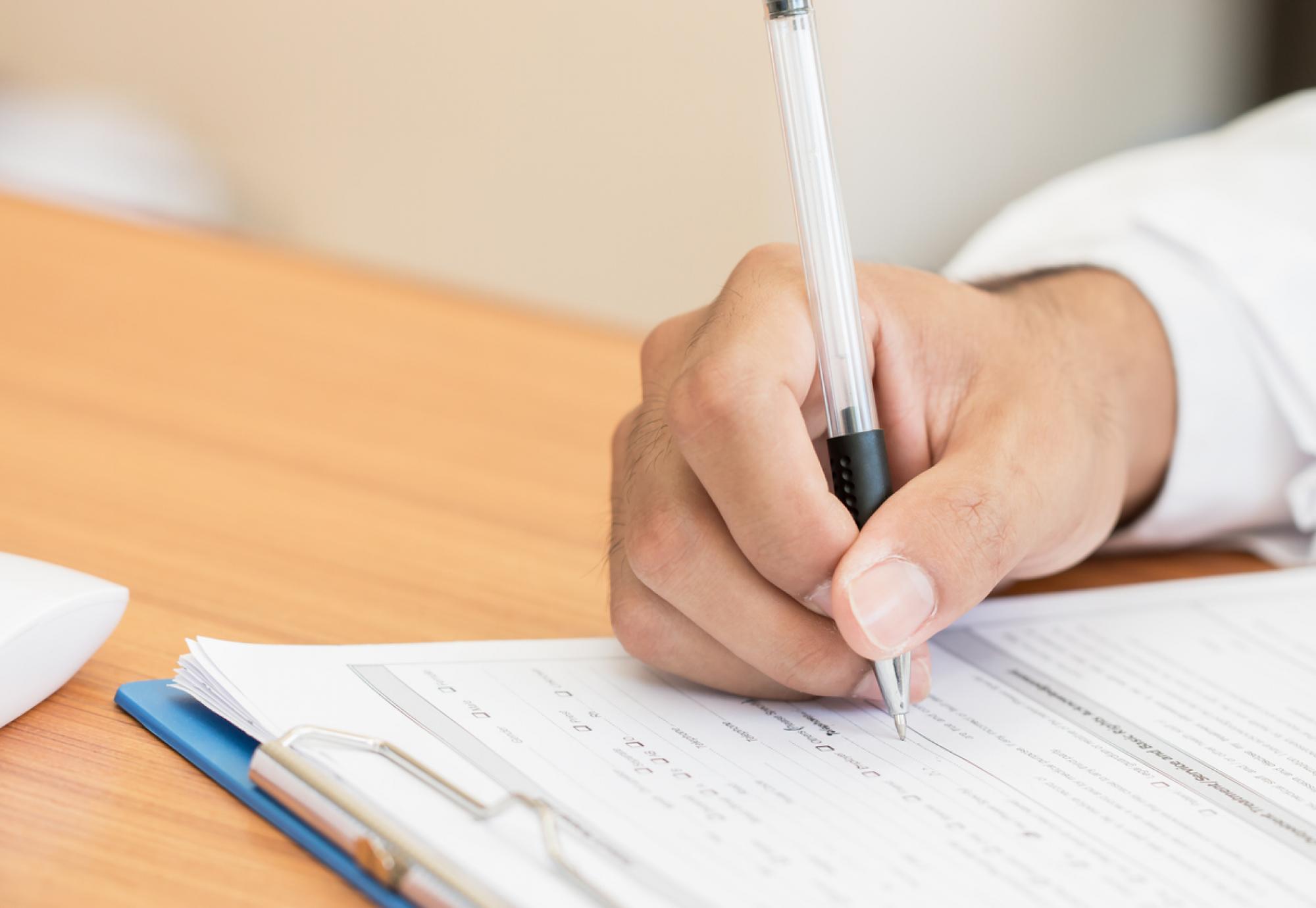 Close-up of a medical professional writing on a clipboard