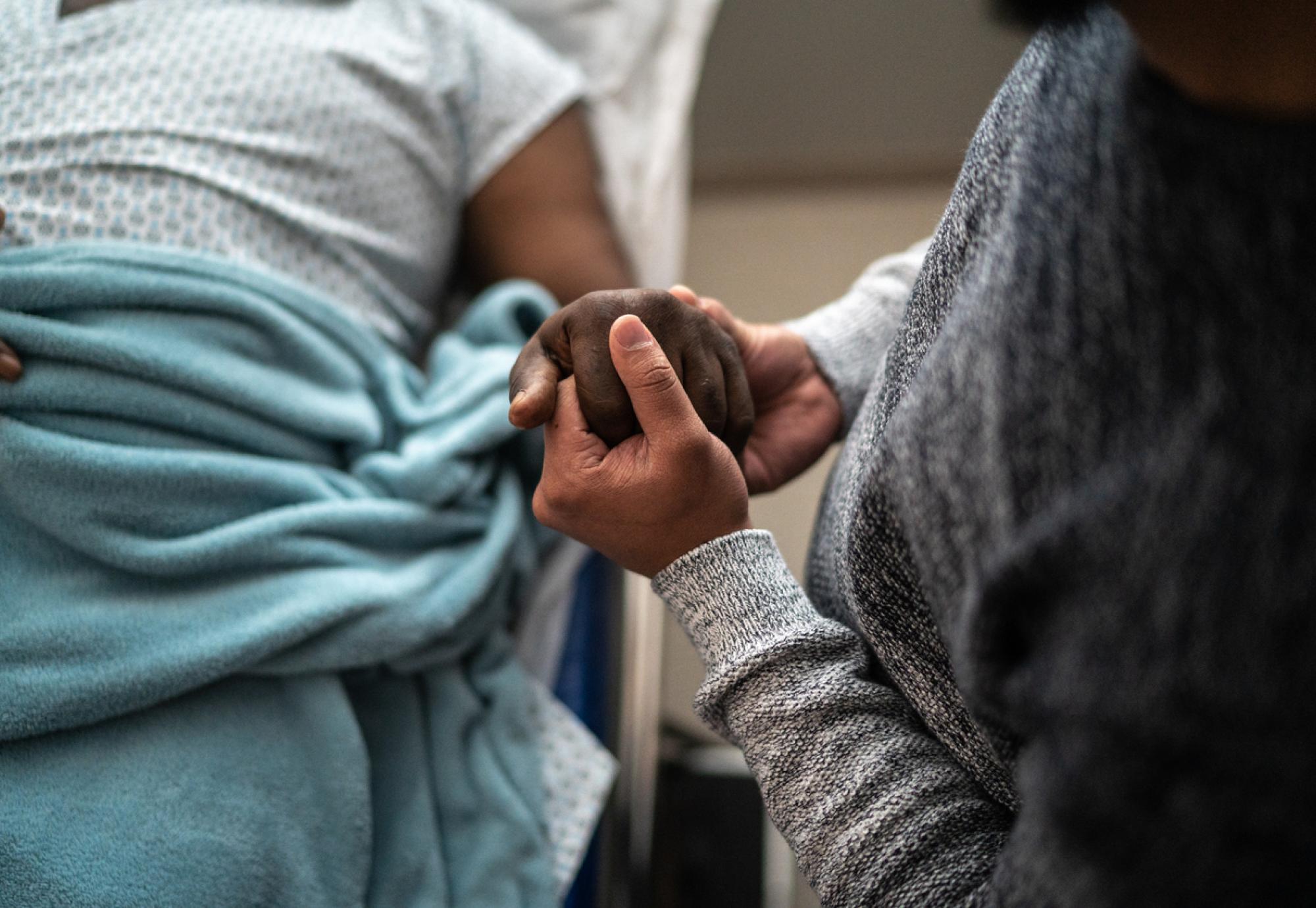 Son holding father's hand at the hospital