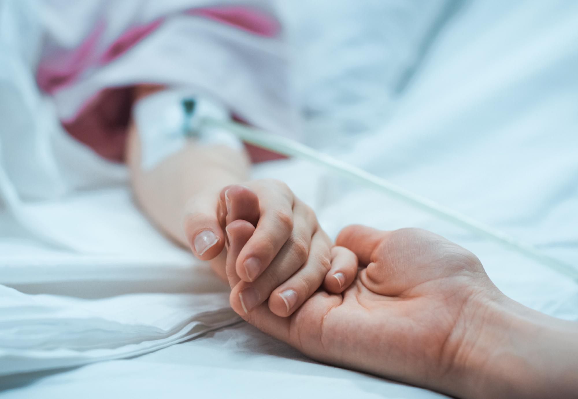 Close-up of a mother holding hands with her child as they recover in hospital