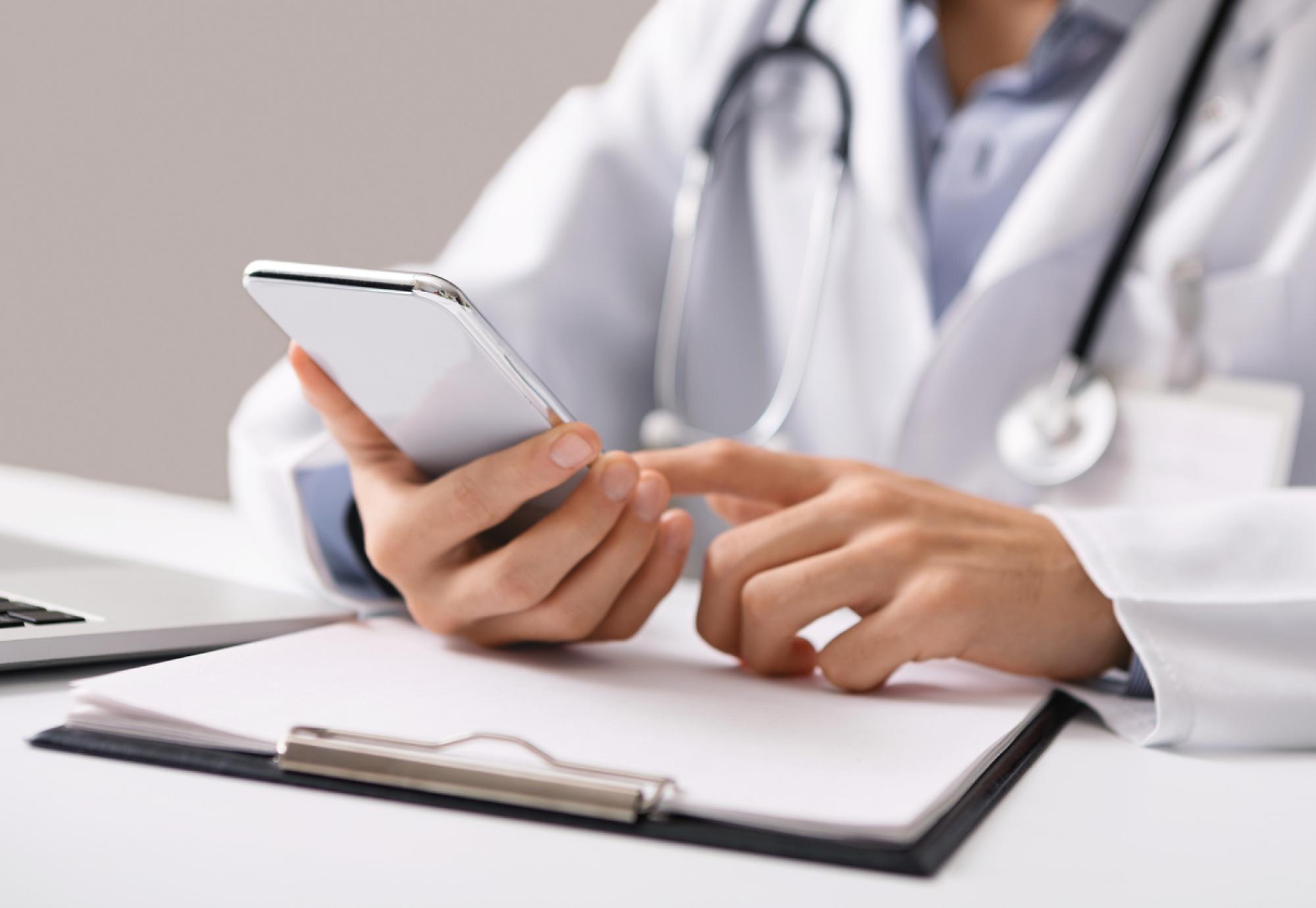 Doctor holding smartphone depicting online GP registration service and digital health