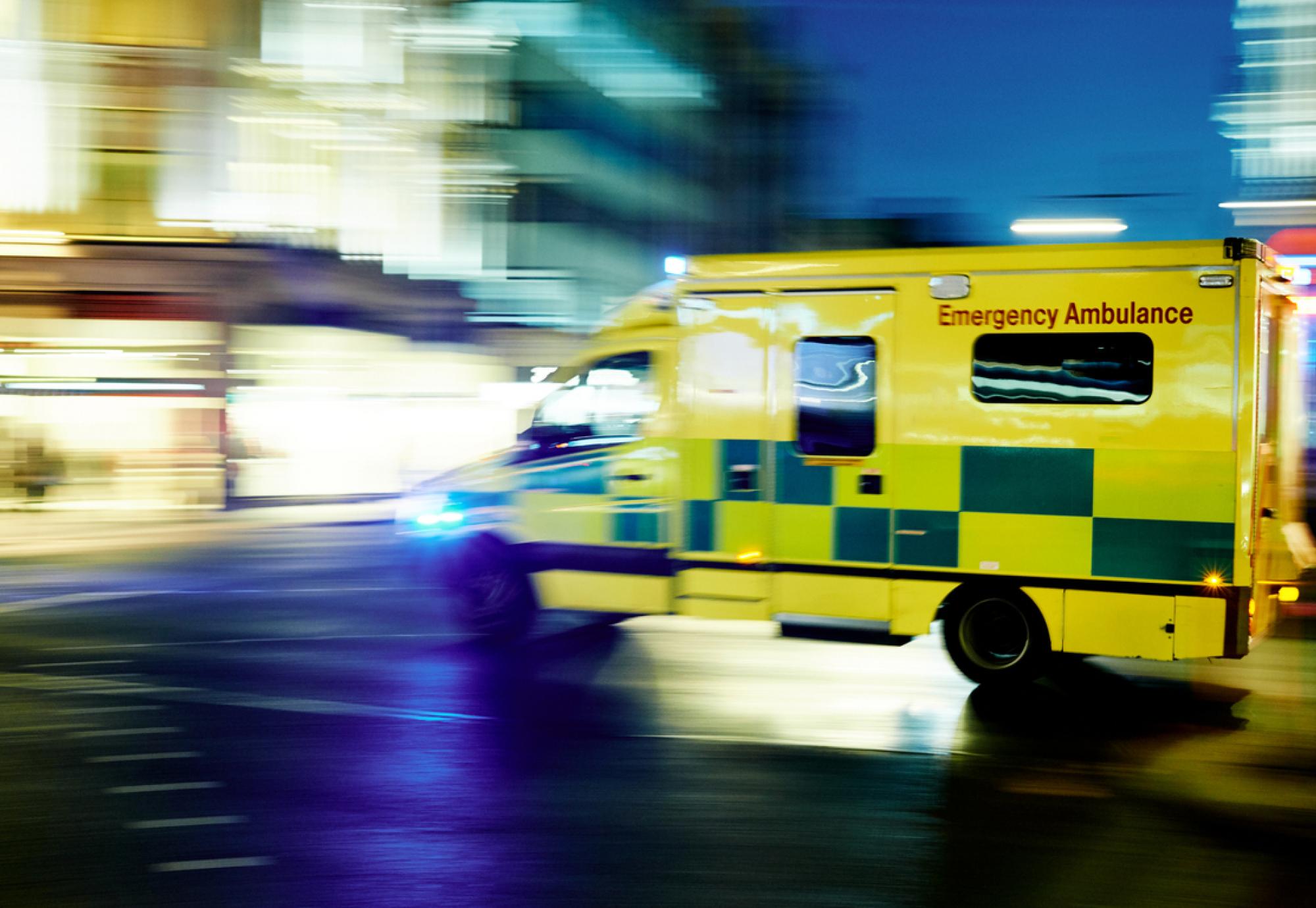 Side view of an NHS ambulance driving past quickly depicting future health emergencies 