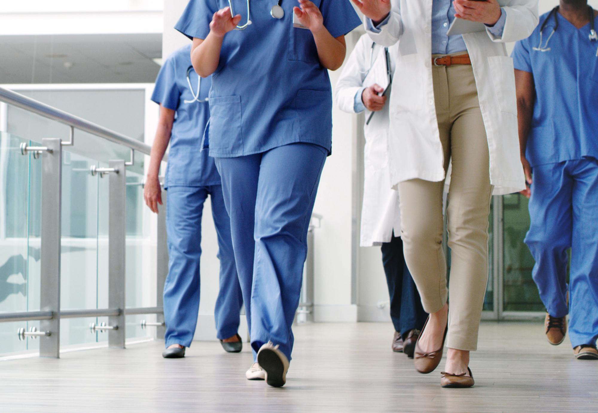 Image of the bottom half of healthcare workers walking down a corridor