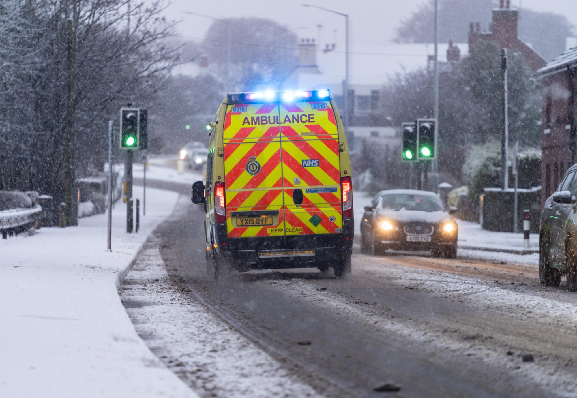 Rear-view shot of an NHS ambulance driving in the snow depicting the Scottish Government's health and social care plan for winter