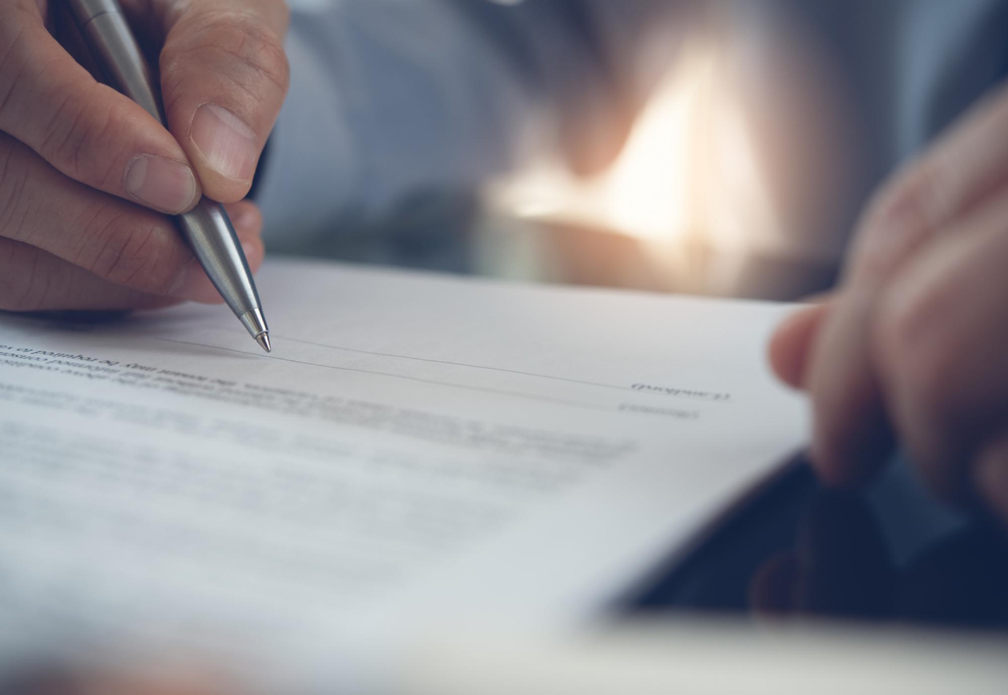 Image of a man signing a contract depicting the new deal for NHS consultants