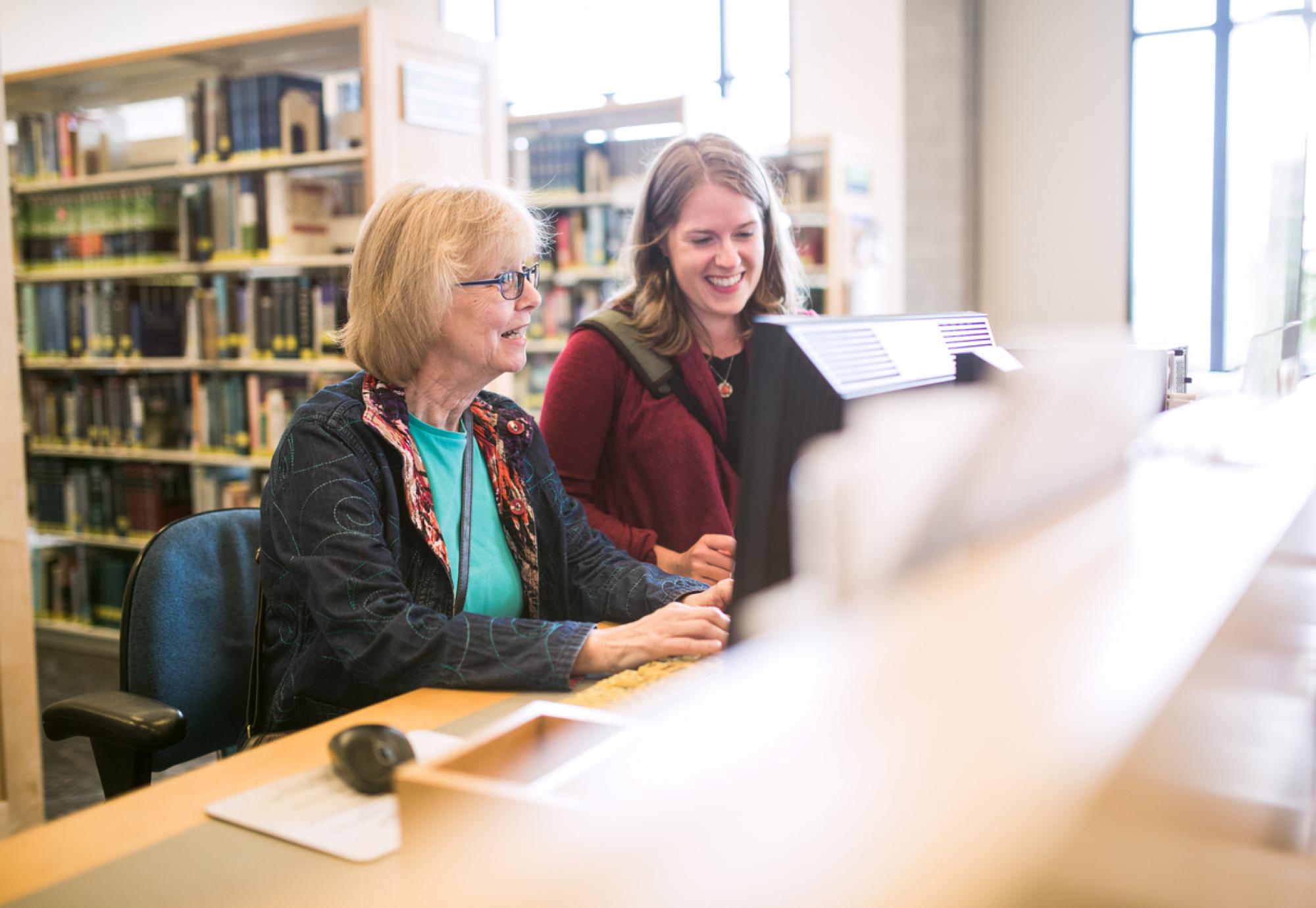 Older woman being helped by librarian to use a computer