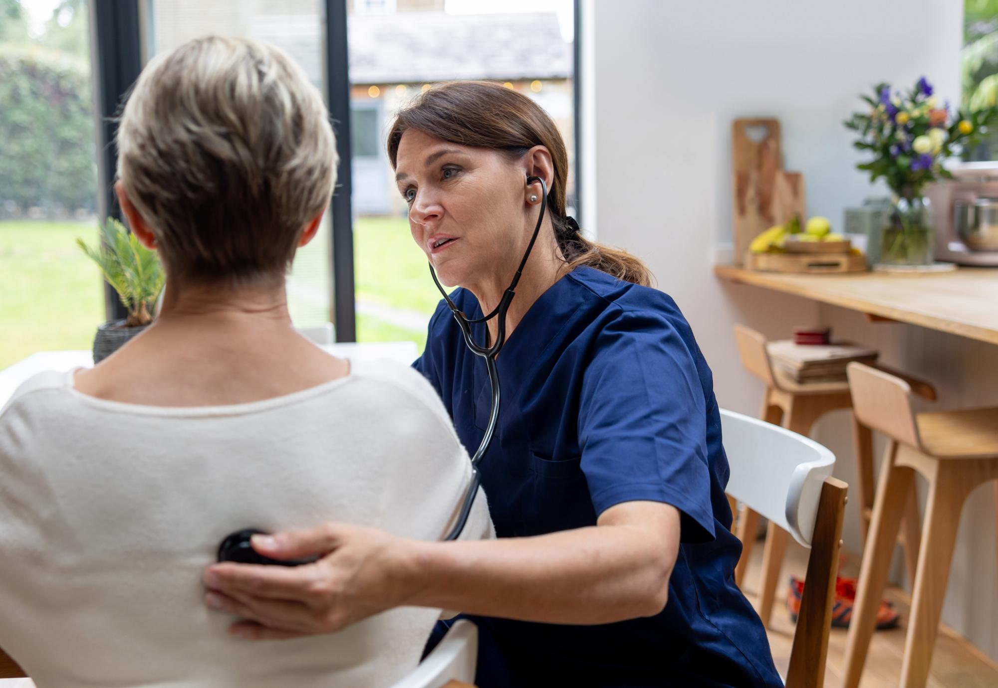Female doctor on a house call listening to the heart of a senior patient with a stethoscope