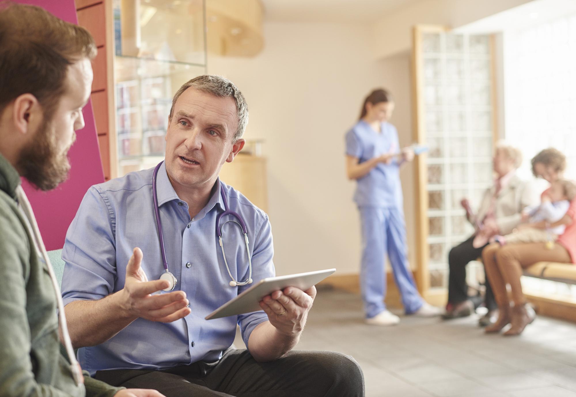 male doctor sits next to a male patient in his waiting room