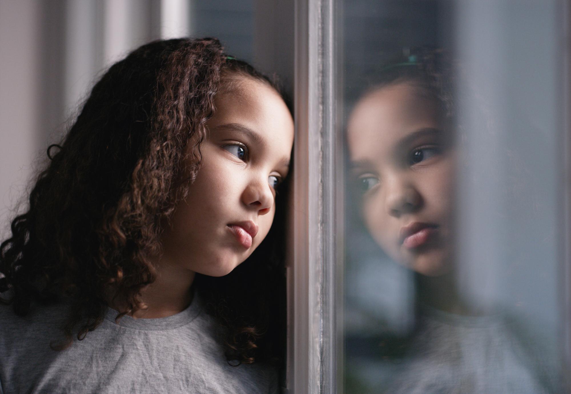 A sad girl looks through a window