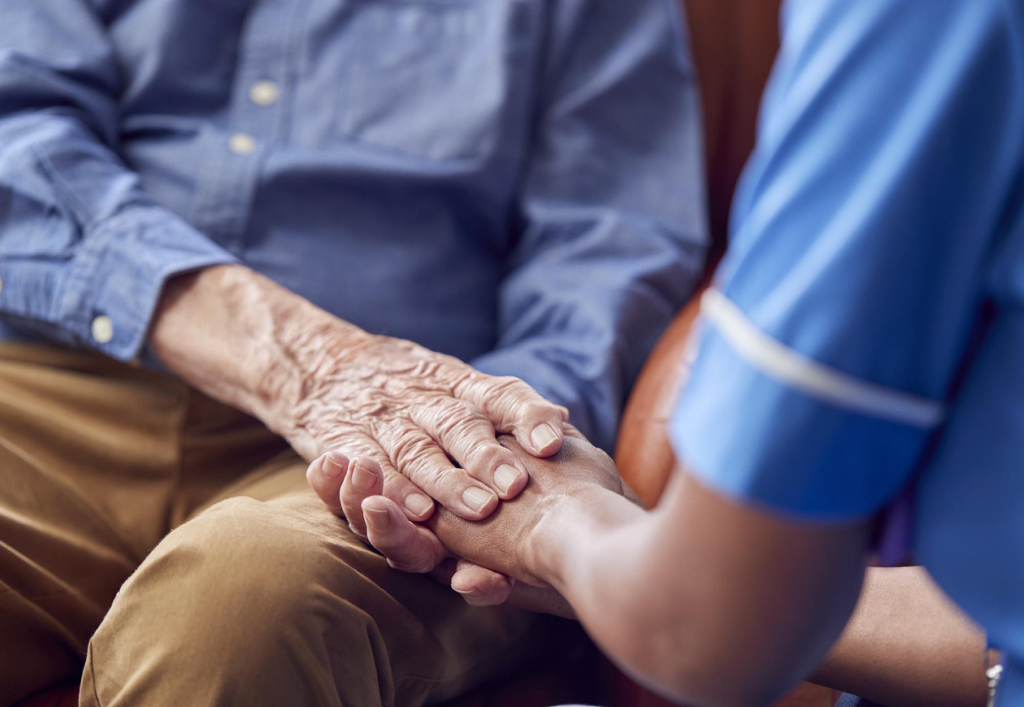 Female Care Worker Holding Hands Of Senior Man