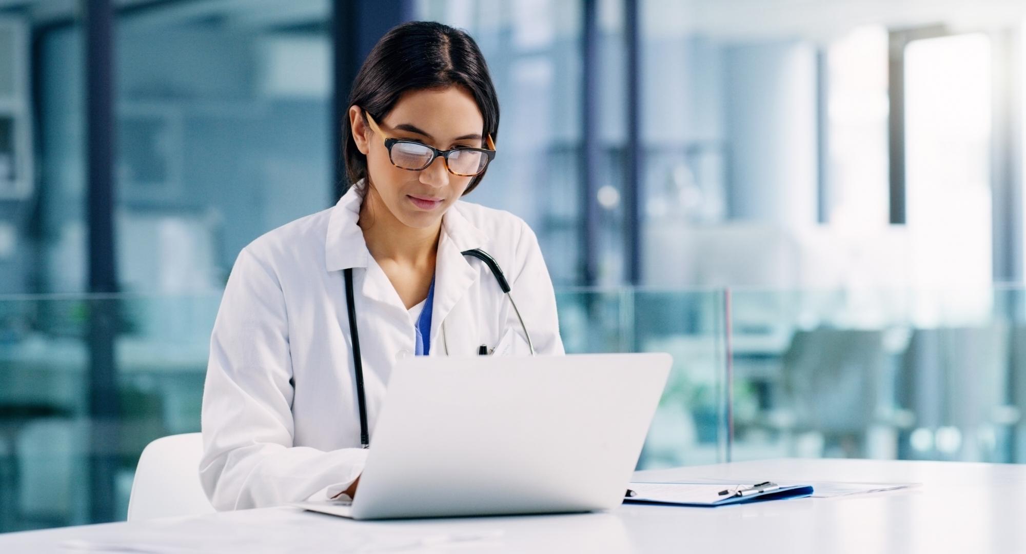 Female doctor looks at medical records on laptop.