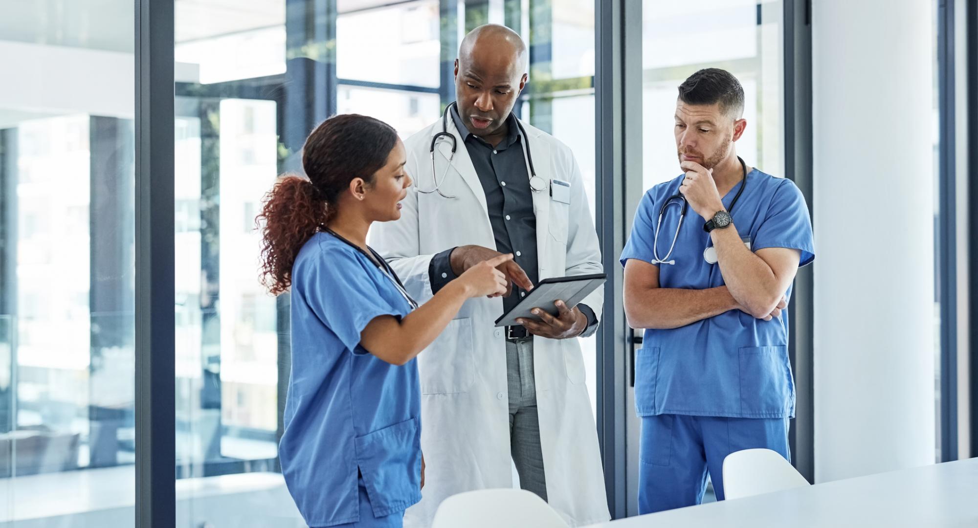 Doctor and two nurses discuss something on a tablet computer