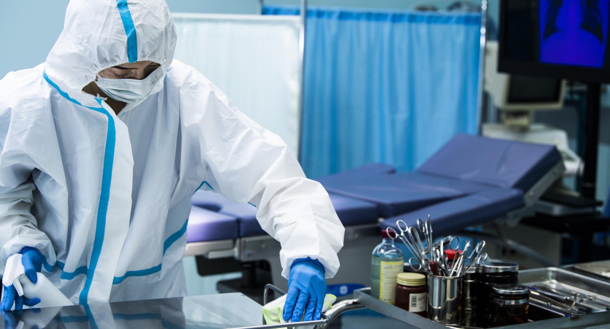 Individual in PPE wiping down a surgical surface