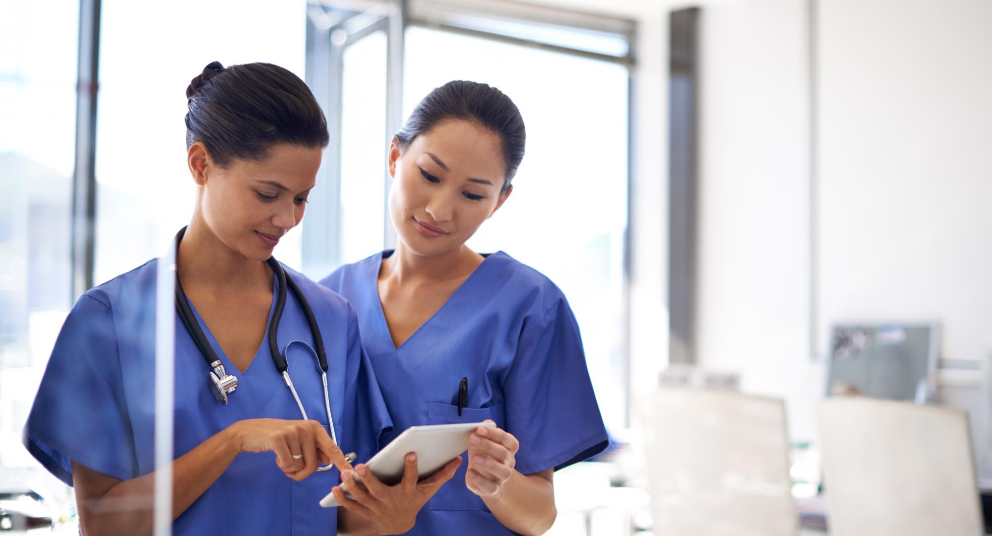 Two nurses discuss while reading a tablet computer