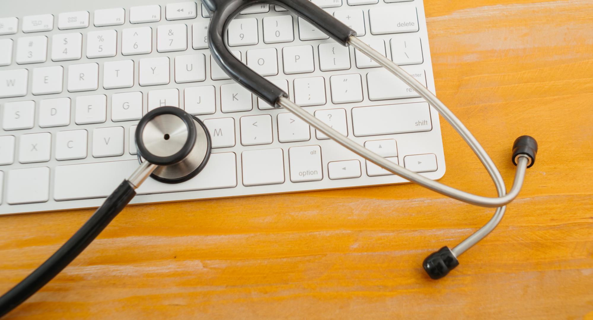 Stethoscope over computer keyboard on orange background