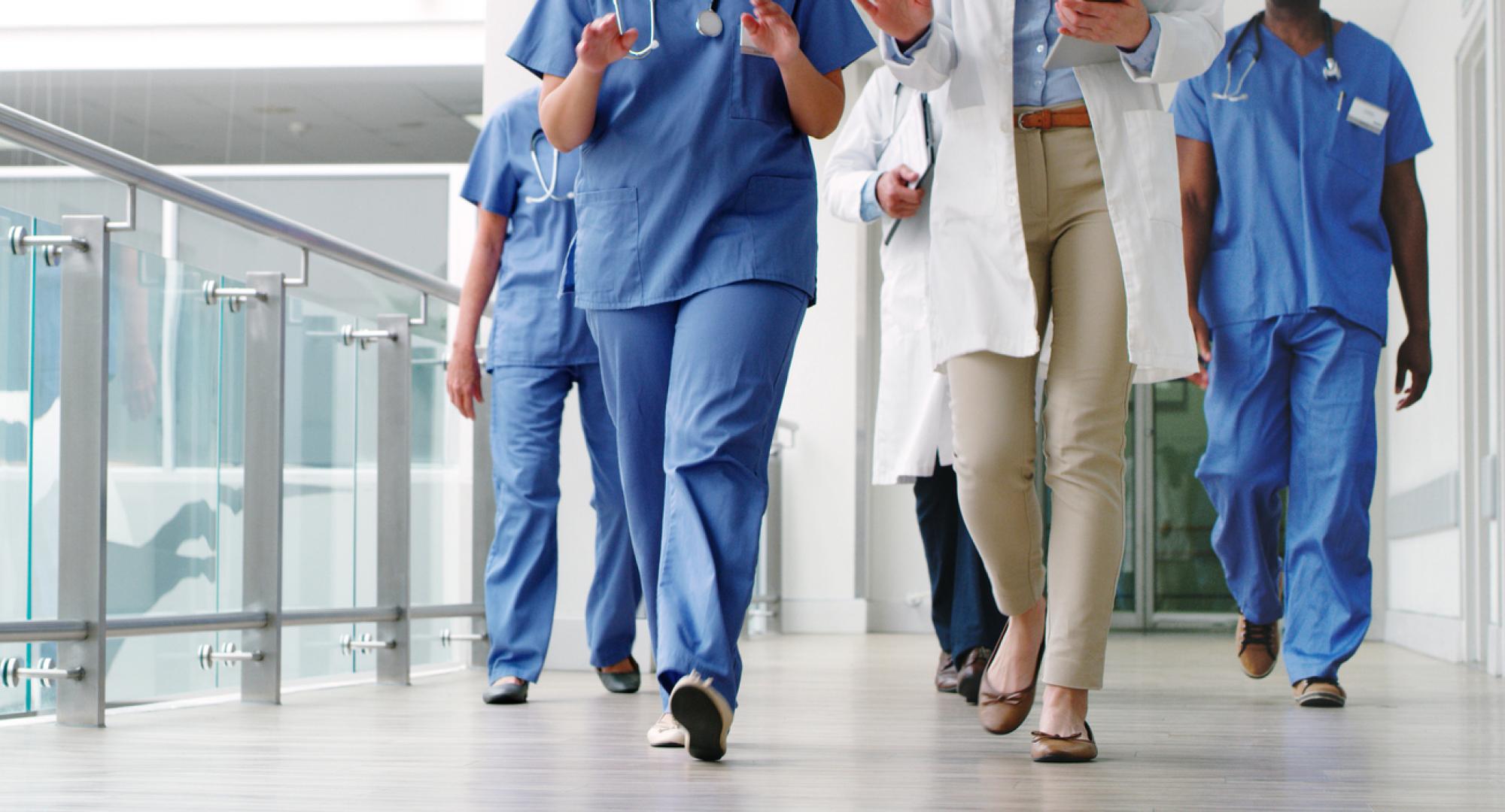 Image of the bottom half of healthcare workers walking down a corridor