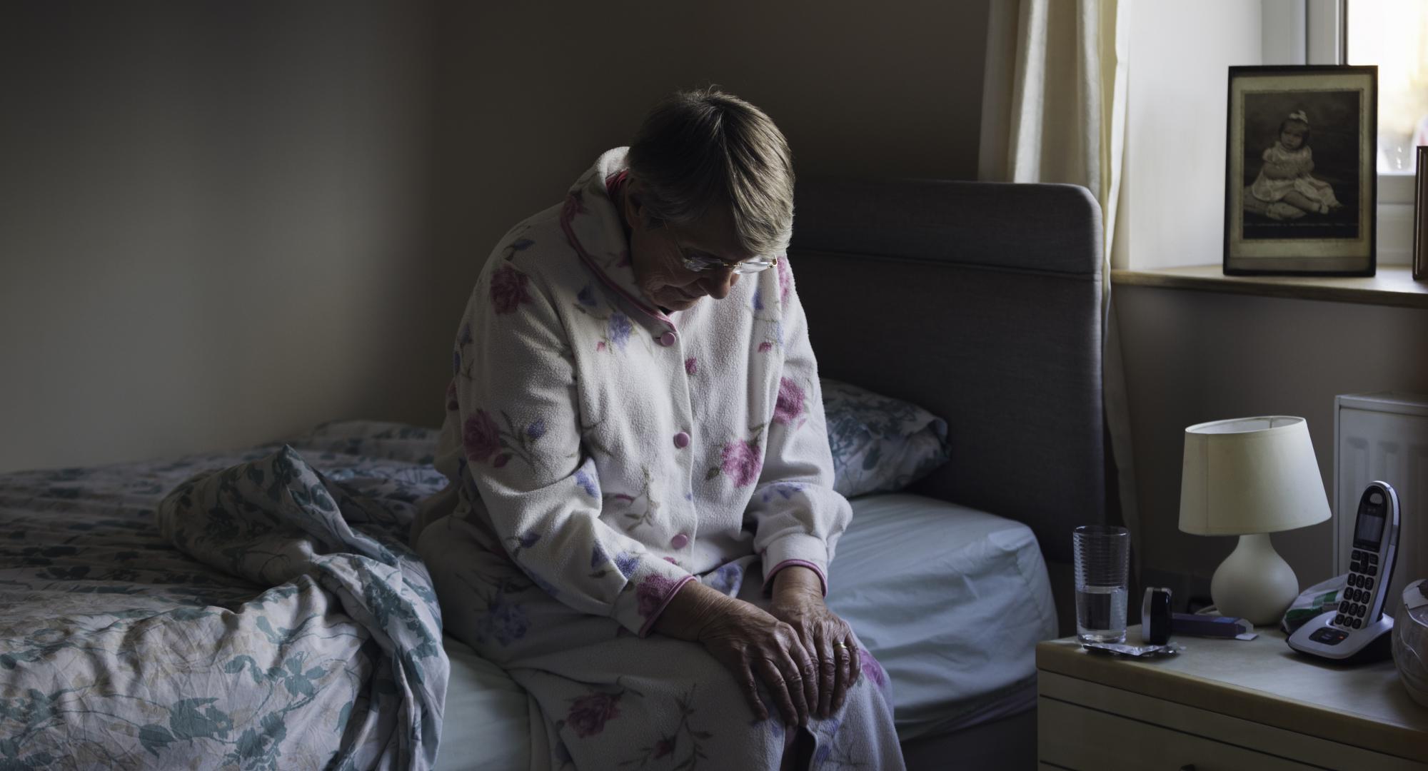 A senior woman sitting on the edge of her bed