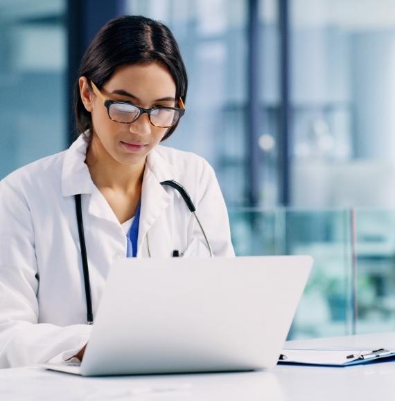 Female doctor looks at medical records on laptop.