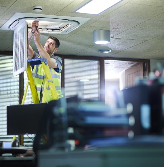 Male engineer on a ladder fixing an air conditioning unit in an office