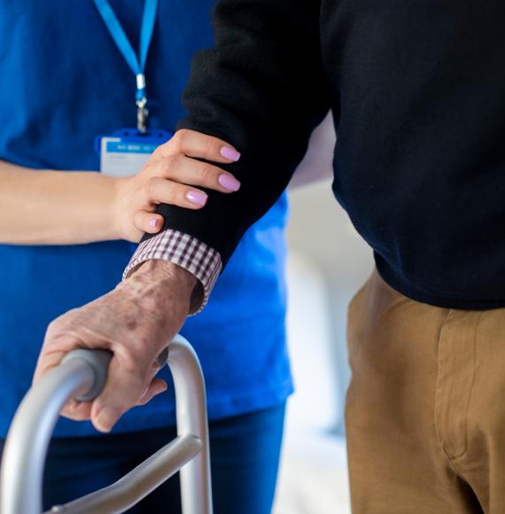 Community care worker supporting elderly person with zimmerframe