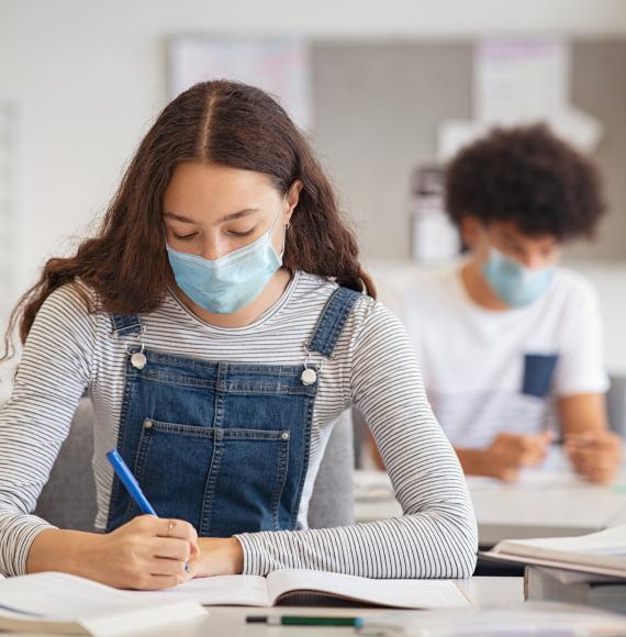 High school or college age girl in mask working at her desk