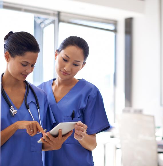 Two nurses discuss while reading a tablet computer