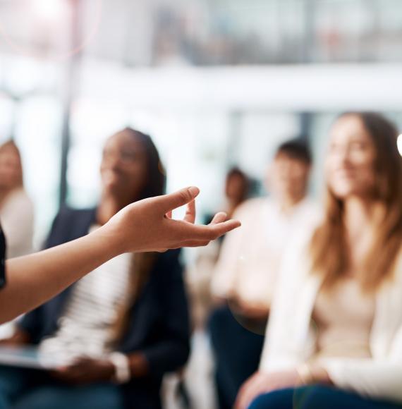 Off picture, woman presenting to a room of colleagues (in soft focus)