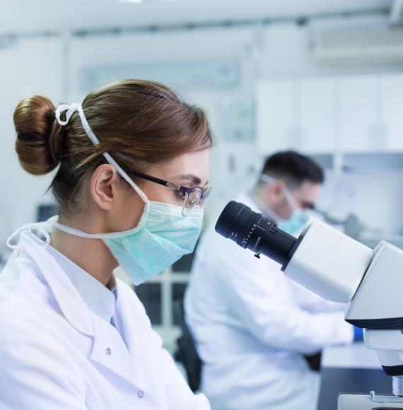 Microbiologist looking down a microscope in a lab