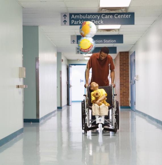 Man pushing boy in wheelchair through corridor