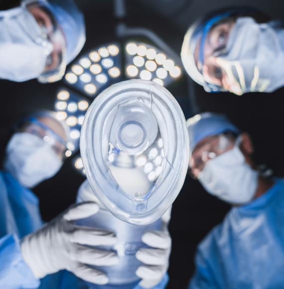 Anesthetist holding oxygen mask above patient in surgery room